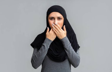 Muslim Woman Covering Her Mouth With Crossed Palms on Gray Background clipart
