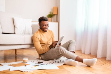 Neşeli adam evde yerde otururken dijital tablet kullanıyor.