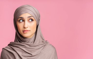 Uncertain arabic woman in hijab biting lip and looking away clipart