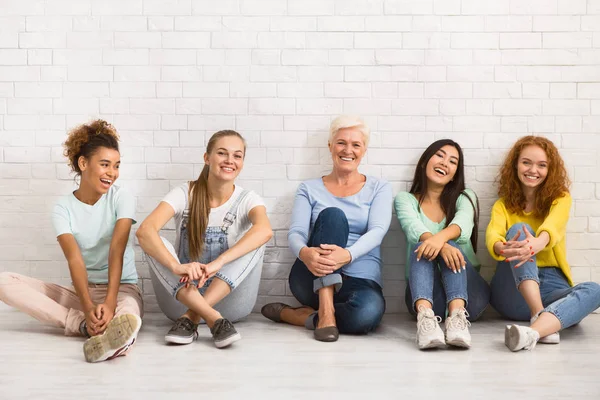 Señoras de diferentes edades sonriendo sentadas juntas en el piso interior — Foto de Stock