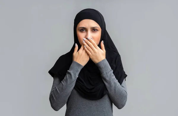 Mujer musulmana cubriéndose la boca con palmas cruzadas sobre fondo gris — Foto de Stock