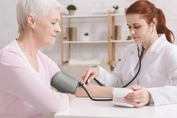 Médico midiendo la presión arterial de una paciente mayor — Foto de Stock