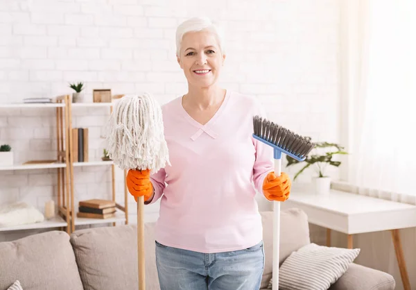 Señora mayor sosteniendo fregona y escoba y sonriendo — Foto de Stock