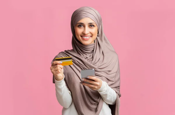 Kredi kartı ve akıllı telefonla tesettürlü mutlu İslamcı kadın. — Stok fotoğraf