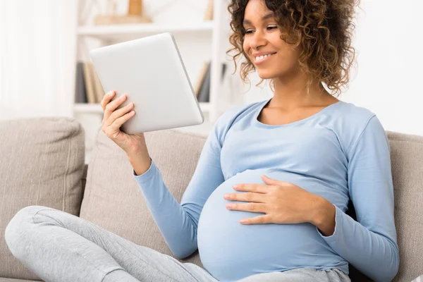 Kobieta w ciąży za pomocą tabletu cyfrowego, spoczywa na kanapie w domu — Zdjęcie stockowe