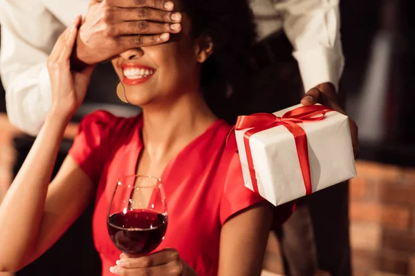 Неузнаваемый бойфренд, закрывающий глаза девушкам, дарящим подарок в ресторане, обрезанный — стоковое фото