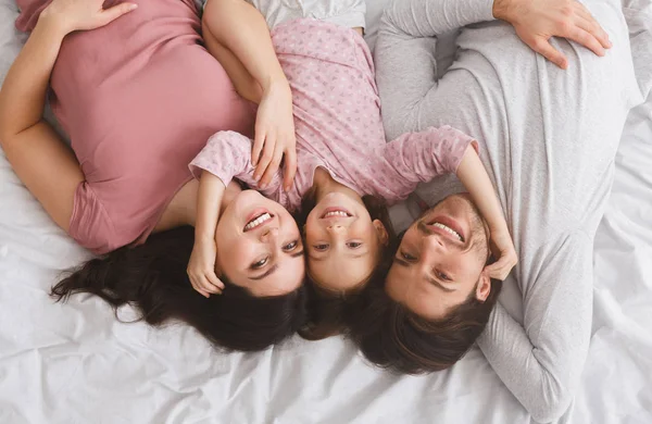 Padres felices y su linda hijita acostada en la cama juntos —  Fotos de Stock