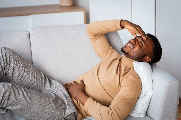 Hombre tocando dolor de estómago y la cabeza acostado en el sofá interior — Foto de Stock