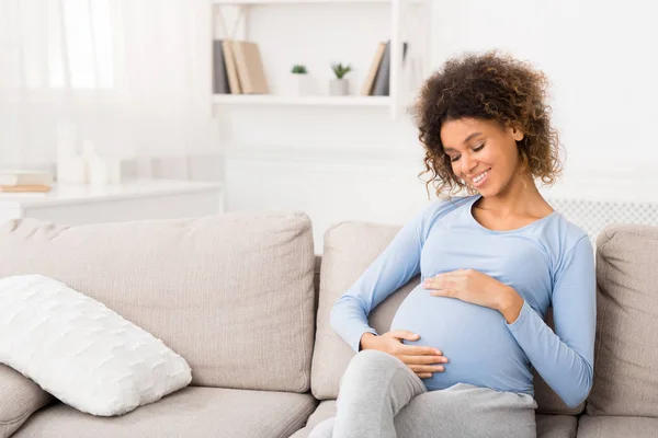 Élvezem a terhességet. Afro lány fogdossa a hasát és mosolyog — Stock Fotó