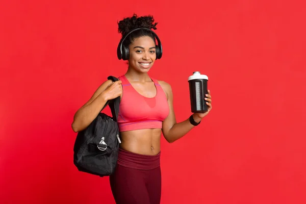 Lächelnde Afro-Frau in Sportbekleidung mit Fitnesstasche und Shaker — Stockfoto