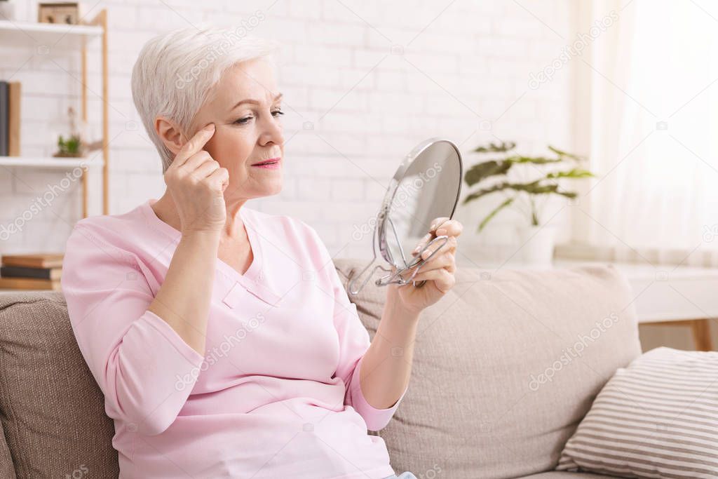Elderly woman looking for wrinkles around eyes at home