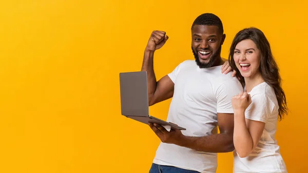 Mutlu ırklar arası çift dizüstü bilgisayarı tutuyor, başarıyı kutluyor ve heyecanla haykırıyorlar. — Stok fotoğraf