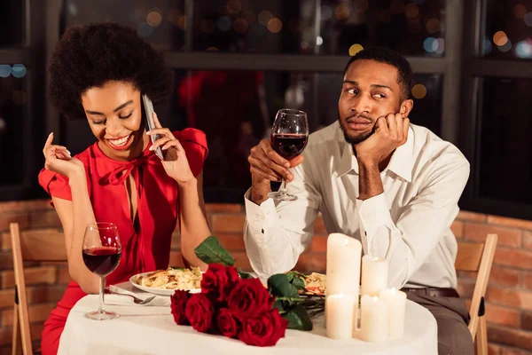 Pojkvännen sitter uttråkad medan flickvännen chattar på telefon i restaurangen — Stockfoto