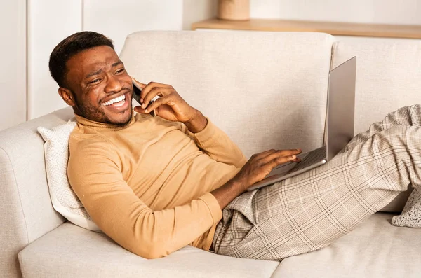 Man Talking On Phone Working On Laptop Lying On Sofa Stock Picture