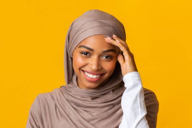 Başörtüsü takmış Afro Müslüman kız utangaç bir şekilde kameraya bakıyor.
