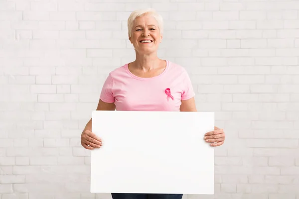 Зрелая леди в футболке с плакатом в руке с раковой лентой — стоковое фото