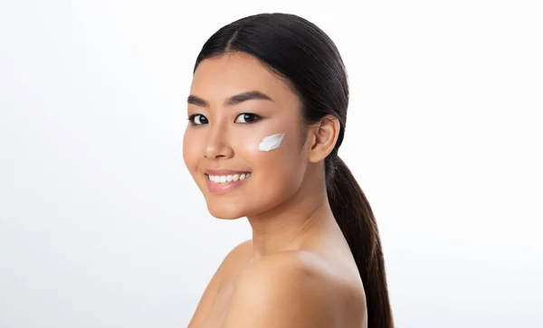 Ansiktsvård. Asiatisk flicka tillämpa grädde på kinden — Stockfoto