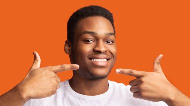 Afro adam gülümsüyor ve sağlıklı dişler gösteriyor.