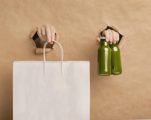 Batido de desintoxicación de jugo verde saludable y manos femeninas sosteniendo una bolsa de papel —  Fotos de Stock