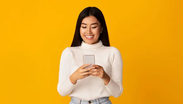 Mosolygós ázsiai lány használ okostelefon sárga háttér — Stock Fotó