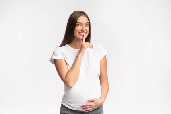 Joyeuse fille enceinte gesticulant doigt sur les lèvres debout, Studio Shot — Photo