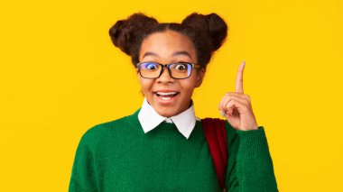 Afro teenager pointing up over yellow studio wall clipart