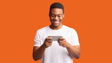 Turuncu arka planda akıllı telefon kullanan Afrikalı bir adam.