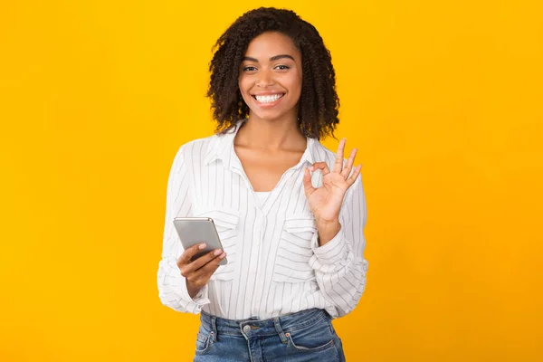 Retrato de una mujer negra sonriente usando el teléfono mostrando un gesto aceptable —  Fotos de Stock
