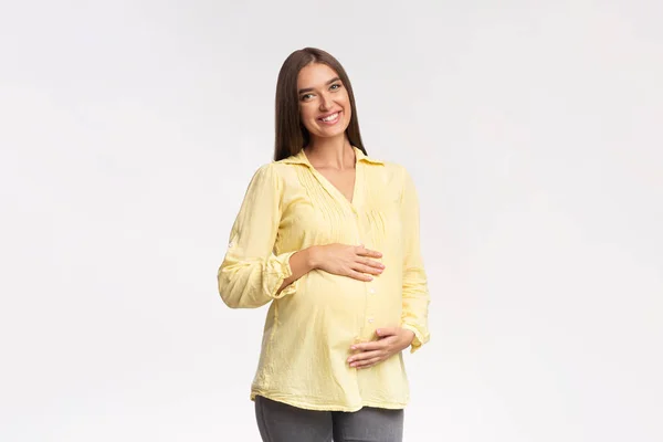 Femme enceinte souriant à la caméra toucher le ventre sur fond blanc — Photo