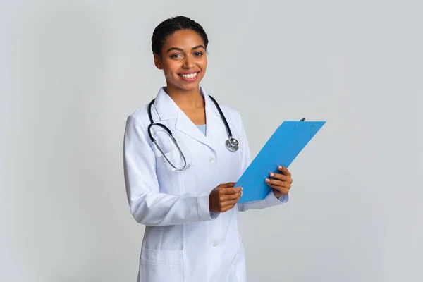 Beyaz önlüklü, elinde panosu olan genç bir afro kadın doktor. — Stok fotoğraf