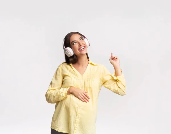 Menina grávida alegre ouvir música em fones de ouvido no estúdio — Fotografia de Stock