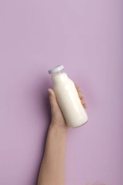 Hand holding bottle with coconut milk over purple background — 스톡 사진