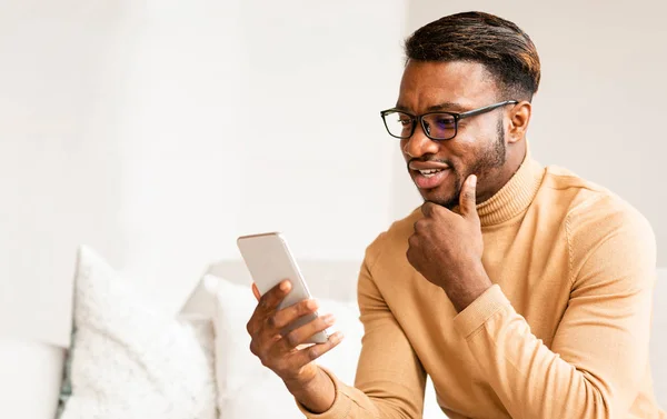 Afro Man met behulp van mobiele telefoon sms zitten op de bank thuis — Stockfoto