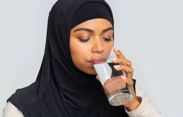 Thirsty black muslim woman in hijab drinking mineral water from glass — Stock Photo, Image