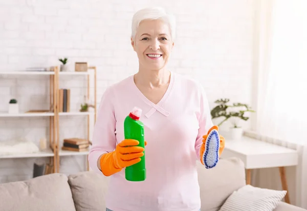 Позитивна старша домогосподарка прибирає будинок пензлем і миючим засобом — стокове фото