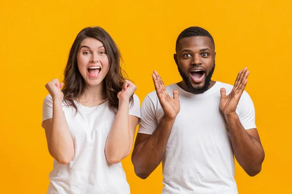 Vielrassiges Paar feiert Erfolg emotional mit erhobenen Händen und offenem Mund — Stockfoto