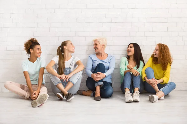 Різноманітні жінки сидять на підлозі розмовляють і посміхаються в приміщенні — стокове фото