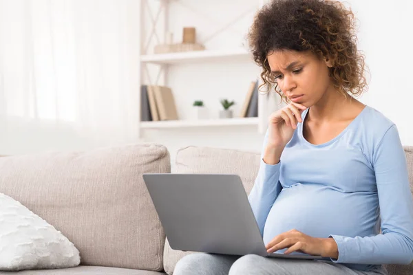 Confundido afro mujer embarazada utilizando el ordenador portátil, la compra de bienes para el recién nacido — Foto de Stock