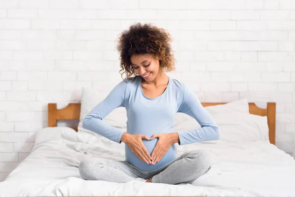 Pregnant woman holding hands in heart shape on baby bump — Stock Photo, Image