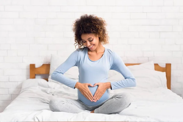 Embarazada mujer cogida de la mano en forma de corazón en baby bump — Foto de Stock