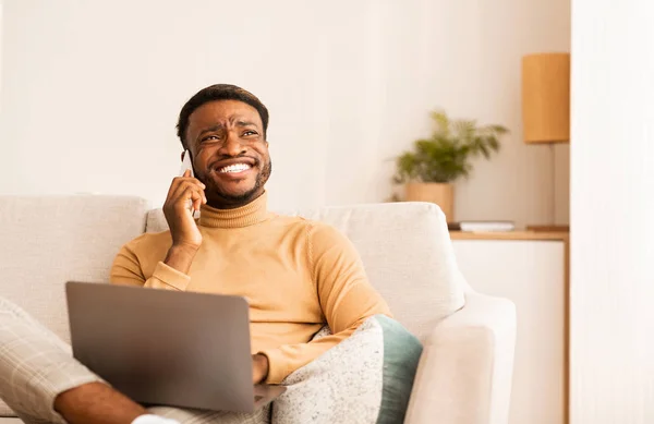 Hombre negro feliz hablando en el teléfono celular trabajando en el ordenador portátil de interior — Foto de Stock