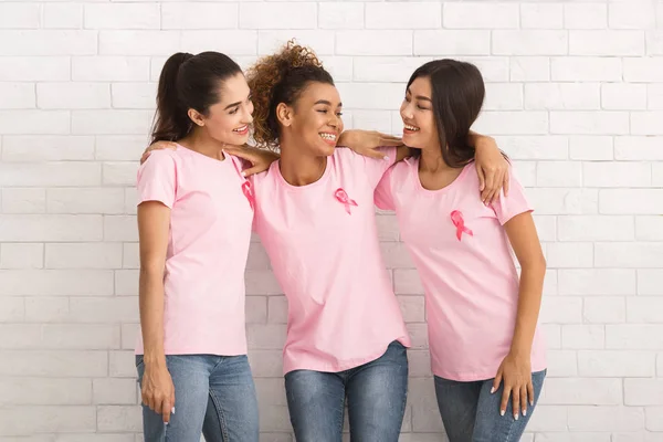 Tres voluntarios en camisetas de cáncer de mama abrazando la pared blanca — Foto de Stock