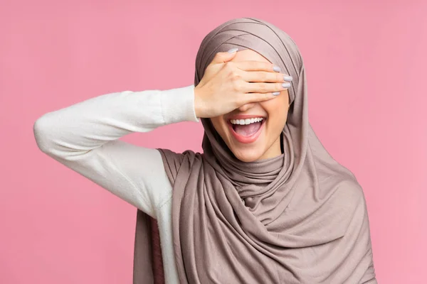 Mujer islámica feliz cubriendo los ojos con la mano y sonriendo, fondo rosa — Foto de Stock