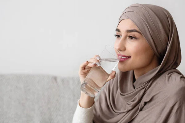 Wanita muda arab dalam jilbab minum air dari kaca di rumah — Stok Foto