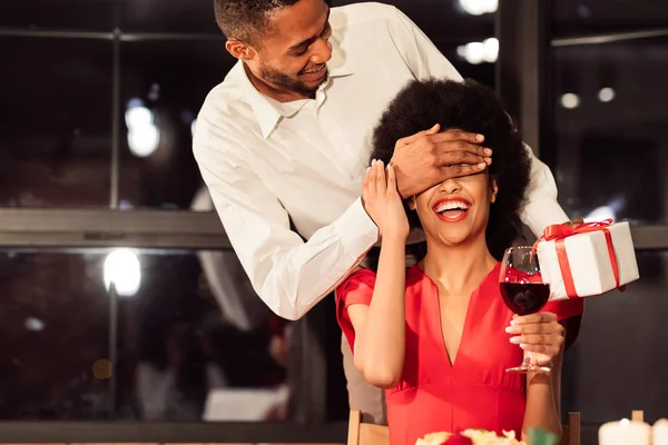 Homem cobrindo namoradas olhos dando presente durante o jantar no restaurante — Fotografia de Stock
