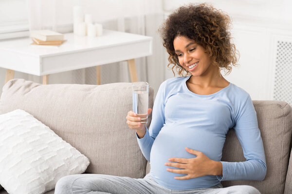 Pregnancy and hydration. Happy woman holding glass of water