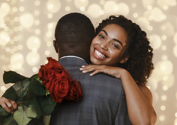 Feliz mujer negra sosteniendo rosas rojas mientras abraza a su hombre — Foto de Stock