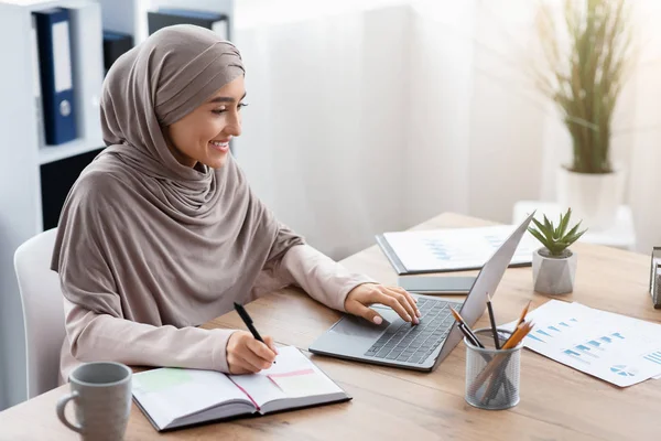 Muszlim nő hidzsáb segítségével laptop és jegyzetel az irodában — Stock Fotó
