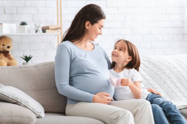 Hamile kadın ve kız göbeğine bebek botları giydiriyorlar.
