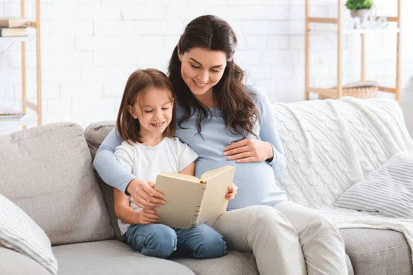 Anaokulu kızı ve annesinin heyecan verici bir kitap okumasını bekliyor. — Stok fotoğraf